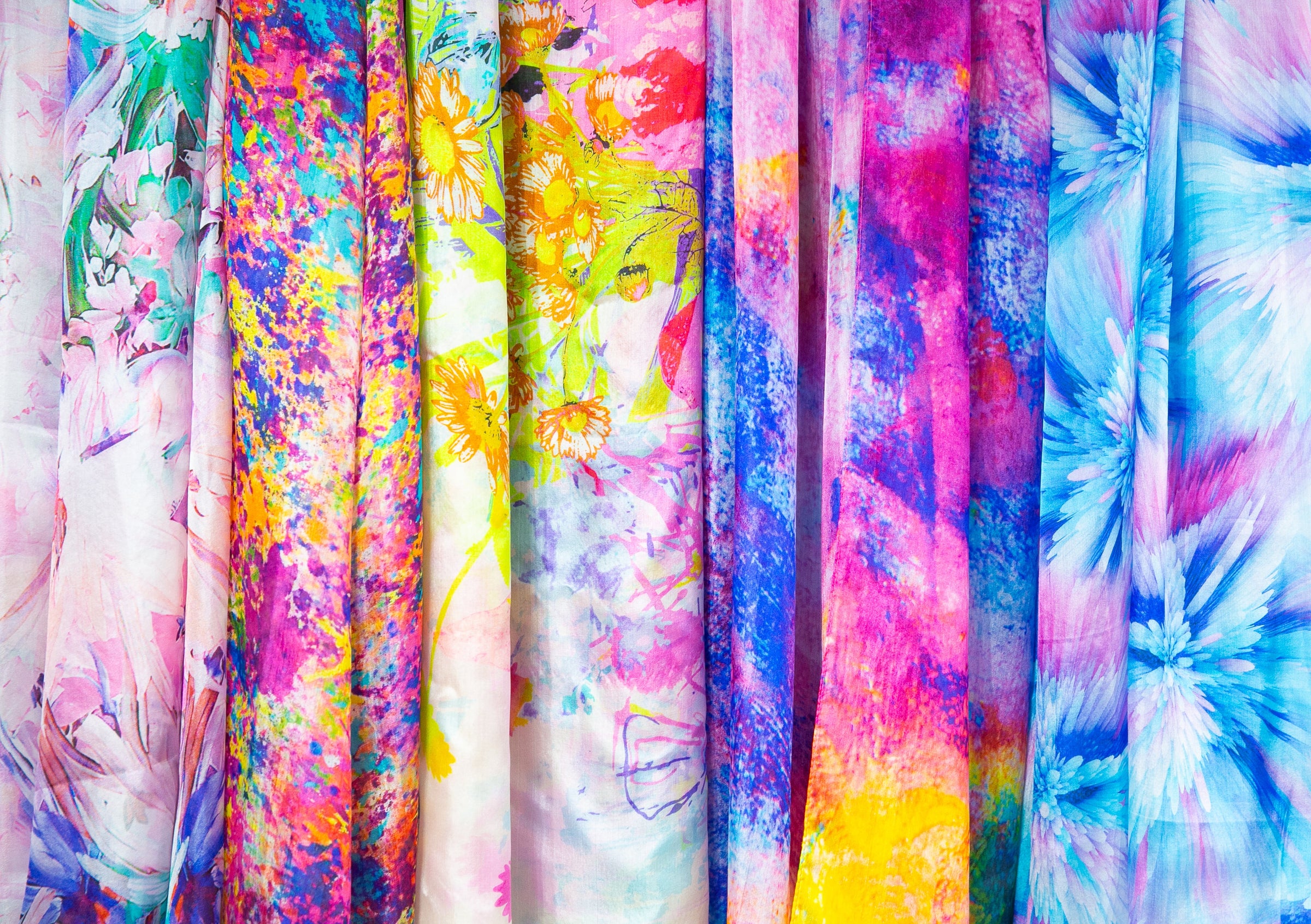 Multiple pure silk scarves hanging in a row, displaying many varieties.