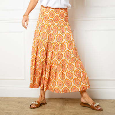 The Flora Stamp Tiered Skirt in orange with a tiered silhouette in a midi length