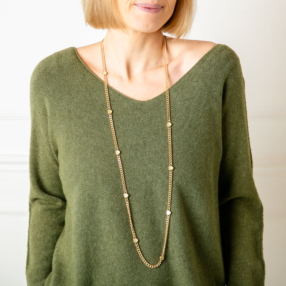 The gold Dayna Necklace featuring small green heart pendants down the length of the chain