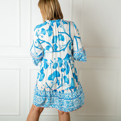 The blue Florence Drawstring Dress with a tie tassel detail and buttons down the front in a bold floral pattern 