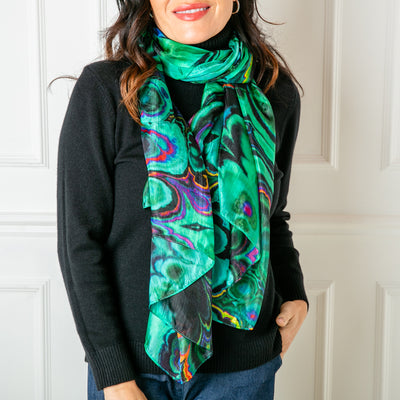 A close up image of the green oil spill silk scarf from Tilley & Grace. Tied elegantly in a loose knot.