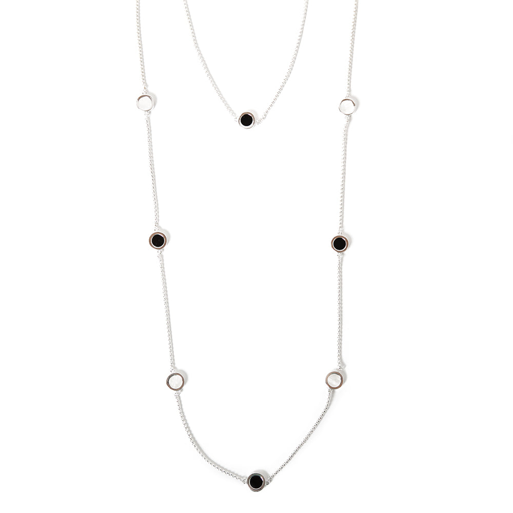 The silver Jasmine Necklace, made up of two chains, one long and one short with circular white and black pendants on them