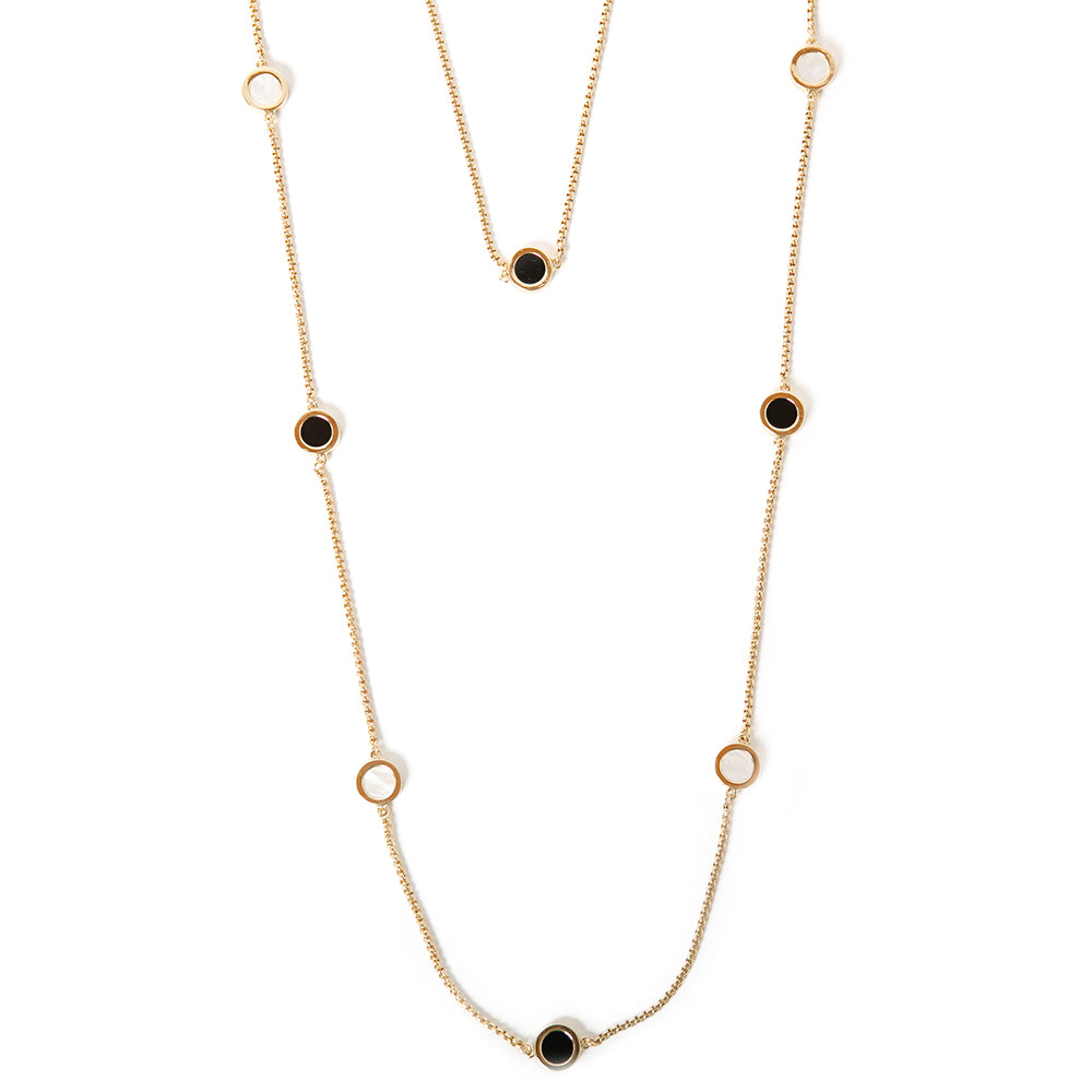 The gold Jasmine Necklace, made up of two chains, one long and one short with circular white and black pendants on them