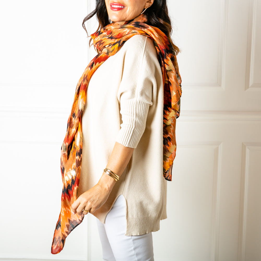 The Phoenix Scarf in orange with hints of metallic gold throughout the pattern