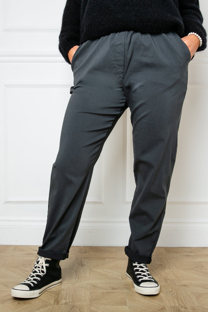 Plus size stretch trousers in charcoal grey with pockets on either side. The bottom hem can be rolled up to any length
