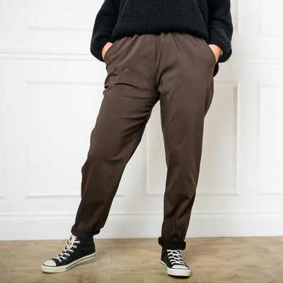 Plus size stretch trousers in chocolate brown with pockets on either side. The bottom hem can be rolled up to any length