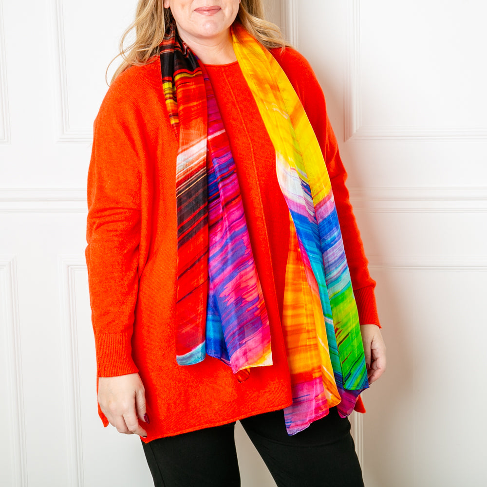 The Rainbow Lights Silk Scarf featuring a vibrant multicolour print with shades of orange yellow red blue purple green and black