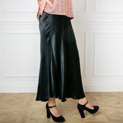 The Satin Slip Skirt in black in a midi length with an elasticated waistband.
