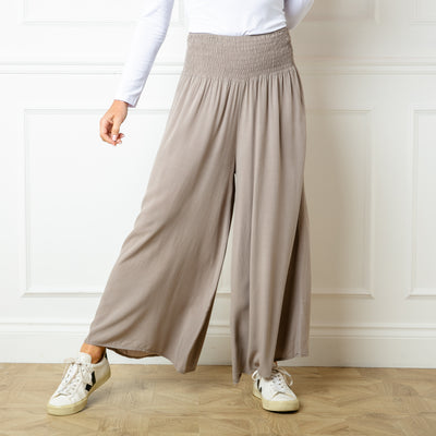 The taupe brown Shirred Waist Wide Leg Trousers with a relaxed loose fitting silhouette around the legs