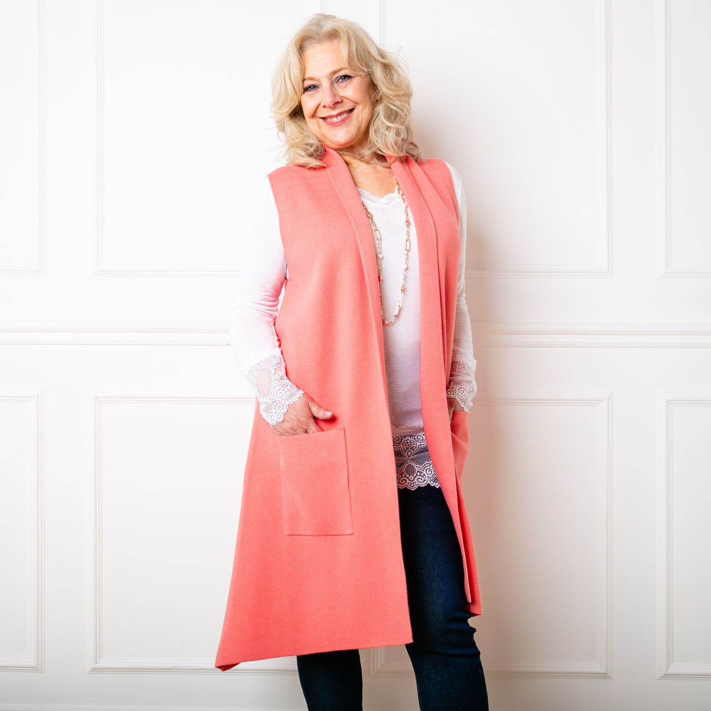 The coral pink Sleeveless Cardigan worn with a lace long sleeve top and trousers.