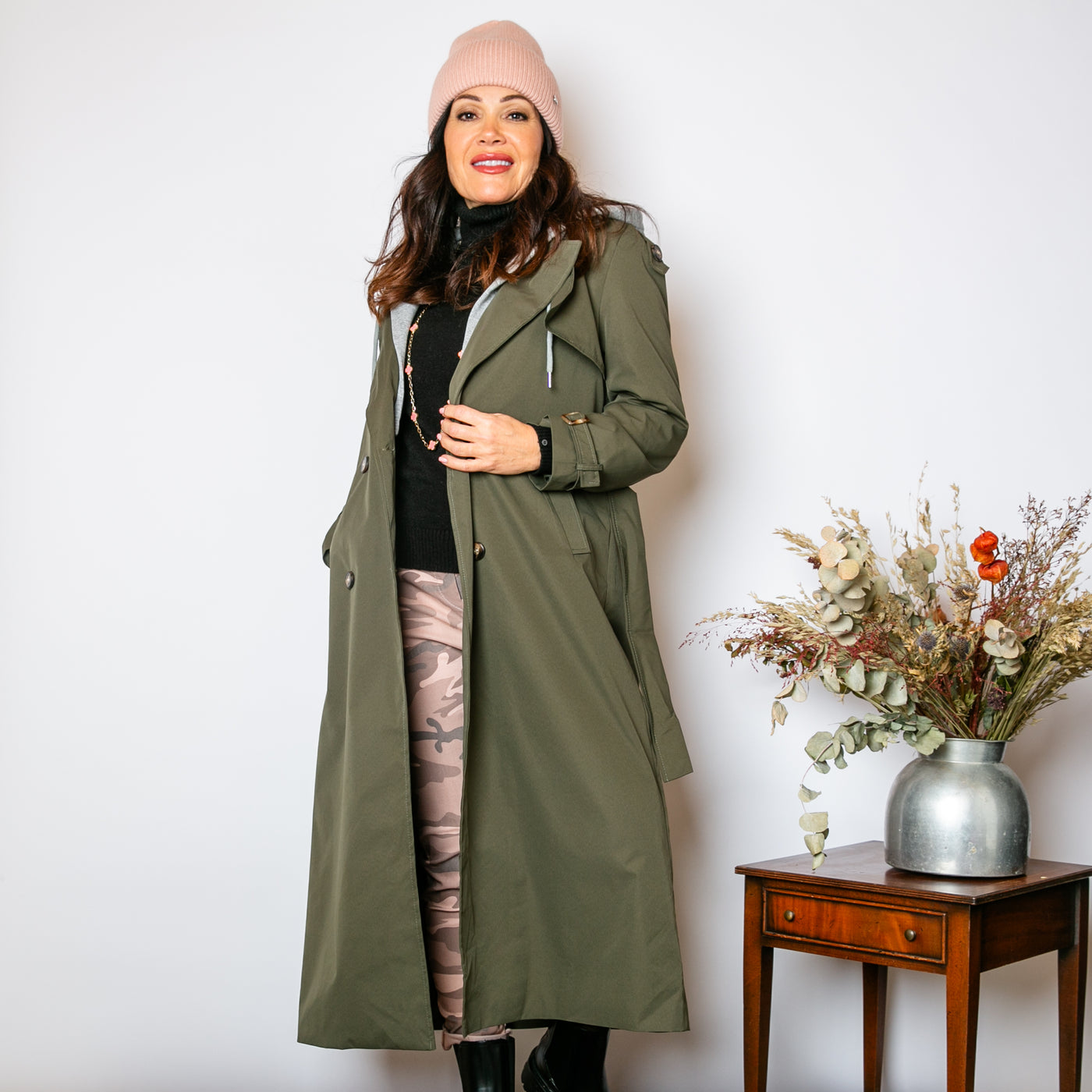 The khaki green Trench Coat With Hood that has a belt to tie around the waist and button fastening