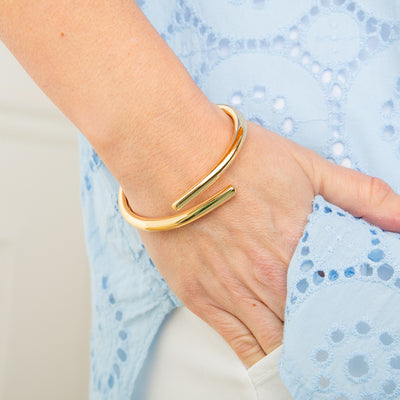 The Verity Twist Bangle in gold made from a chunky plated metal with a hinge fastening for easy wear
