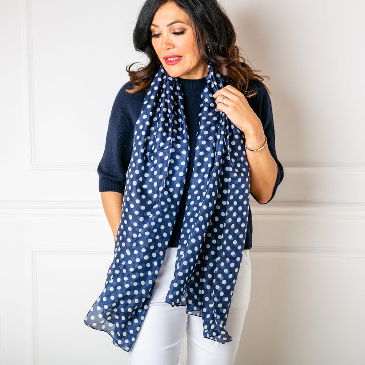 The Navy Polka Dot Silk Scarf worn loosely around the neck