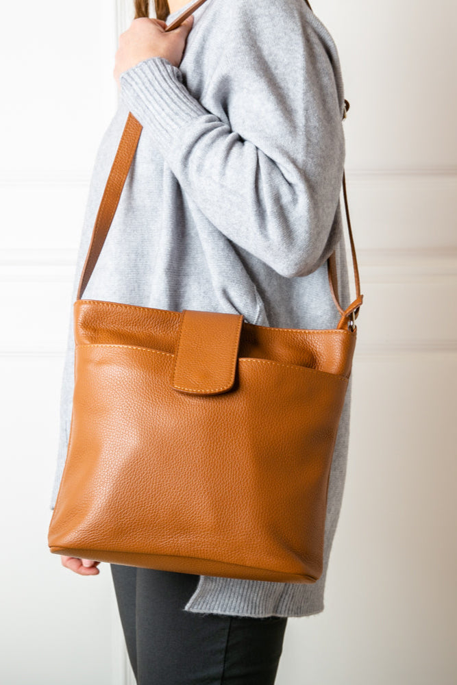 A model wearing the Pimlico Handbag in brown tan colour, shown from the front and including the adjustable leather strap, the fold over presstud fastening and the outside pocket. Made from Italian leather.