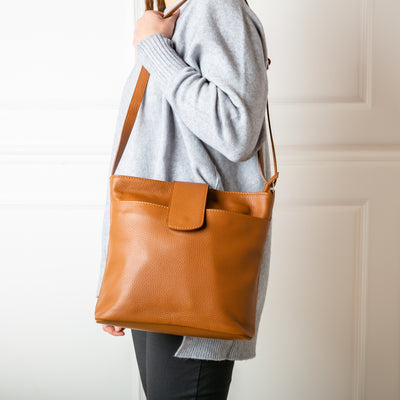 A model wearing the Pimlico Handbag in brown tan colour, shown from the front and including the adjustable leather strap, the fold over presstud fastening and the outside pocket. Made from Italian leather.