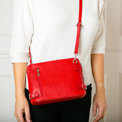 Model shot of Sloane Handbag in red, shown from the front, including the adjustable leather strap, three side zip fastening, buckle detail and the outside pocket. Made from Italian leather.