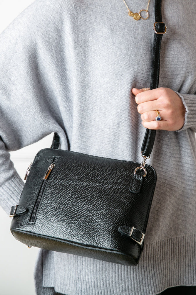 Model shot of  Italian leather Sloane Handbag, in black, with adjustable leather strap, three side zip fastening, buckle detail and the outside pocket. Shown from the front.