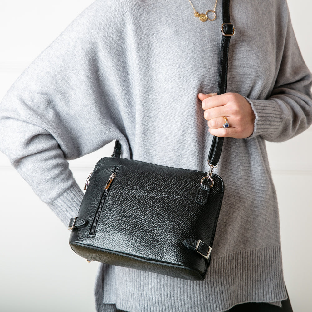 Model shot of  Italian leather Sloane Handbag, in black, with adjustable leather strap, three side zip fastening, buckle detail and the outside pocket. Shown from the front.